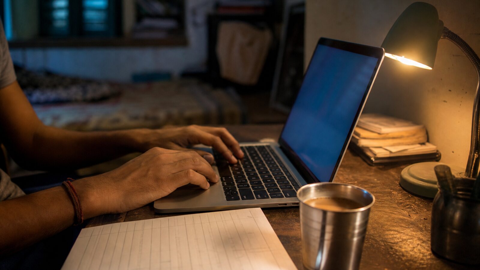 A student’s hands on a laptop at night, chai nearby, a handwritten weekly practice plan on the desk.